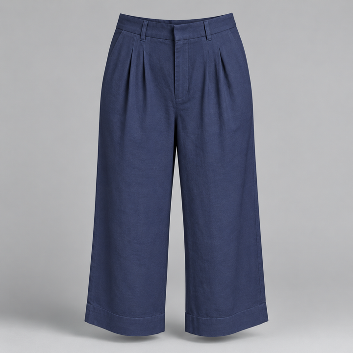 A pair of navy blue cropped trousers with pleated front details and rolled cuffs, displayed on a neutral gray background.